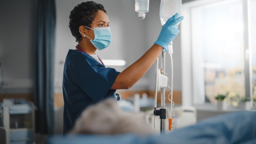 african american female nurse checking an IV bag for a patient